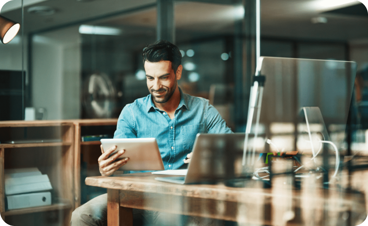 Man sitting at a desk in a modern office while browsing his tablet Man sitting at a desk in a modern office while browsing his tablet