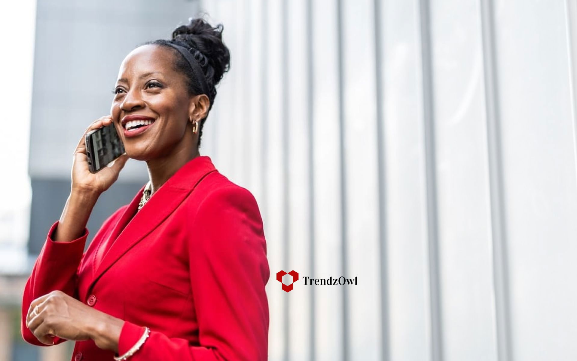 A person in a red suit speaks on a phone, smiling. text on the image reads "trendzowl."