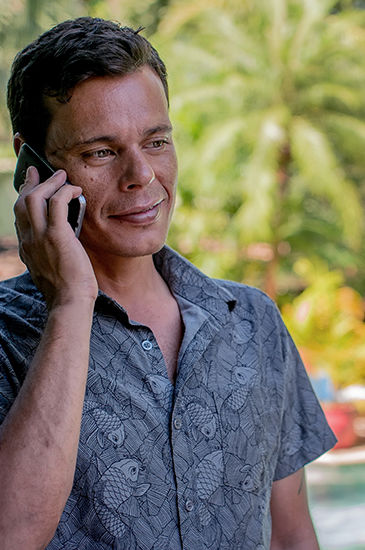 Man in patterned shirt smiling while talking on a mobile phone outdoors. Man in patterned shirt smiling while talking on a mobile phone outdoors.